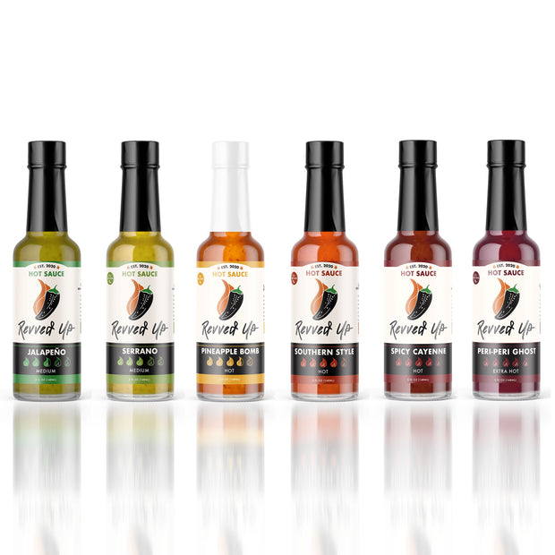 Unleash your inner daredevil with our six original hot sauces. Free shipping if you try all six. Each sauce features a unique mix of peppers and spices. From medium to extra hot, these bold blends will add flavor to any dish!  From peppers such as Serrano, Peri-Peri, and different flavors such as tropical and smoky, each bottle creates its own unique flavor. We hope Revved Up makes you feel inspired to take more risks and spice up your life! White background. 