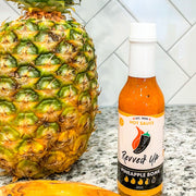 Pineapple Bomb Hot Sauce - | Revved Up. Pineapple Bomb Hot Sauce. Made with real pineapples instead of the artificial stuff typically found in other hot sauces, this zesty mixture gives your boring food new life while giving a tropical sweetness with a medium-high heat that will have your mouth watering for more. Kick up lunches such as chicken sandwiches and burgers or add some flavor to traditional Mexican dishes like burritos and tacos! Pineapple bomb hot sauce in the kitchen next to a pineapple. 